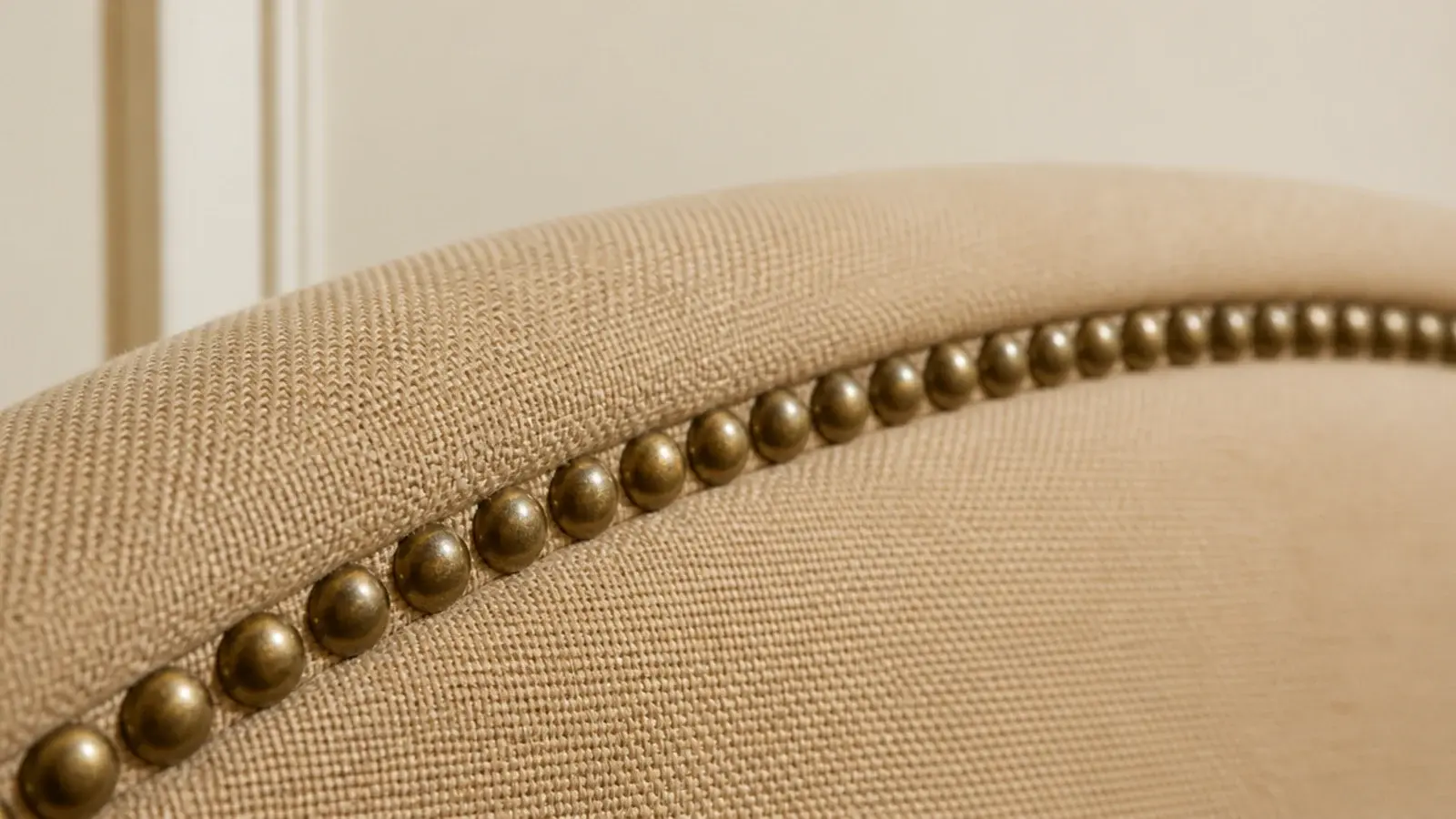 antique brass nailhead trim outlining a plain sand upholstered headboard