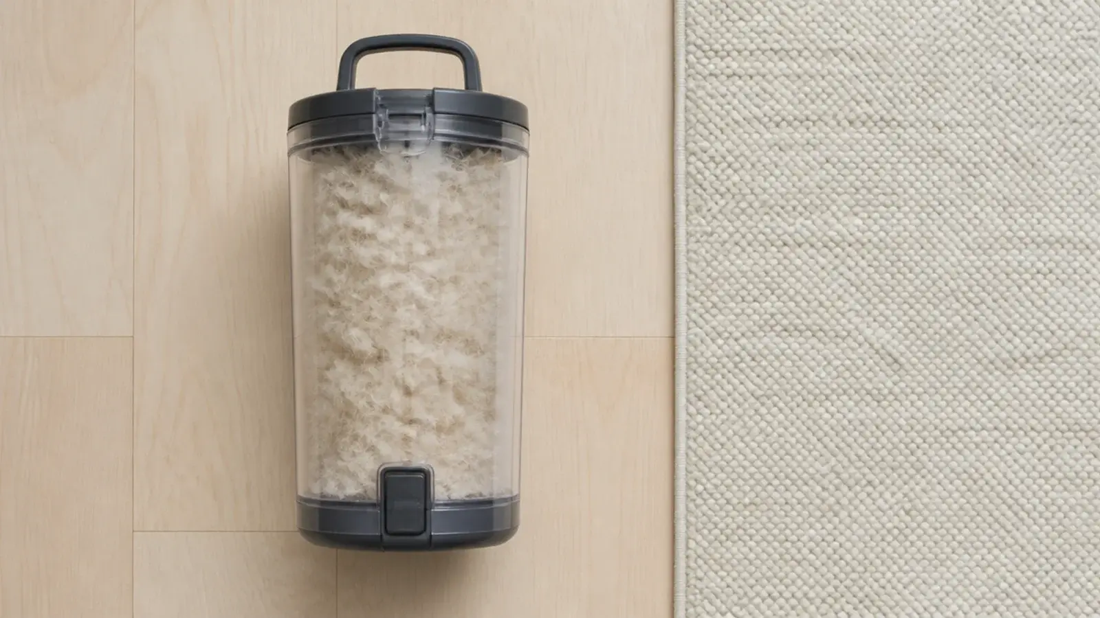 loose wool fibres collected in a vacuum canister beside a rug