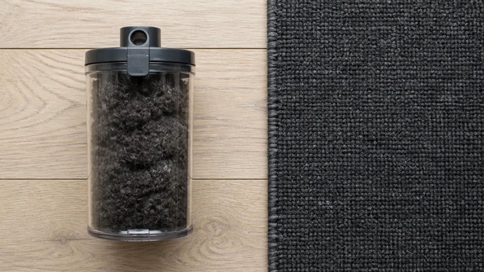 vacuum canister filled with dark wool fibres beside a new rug