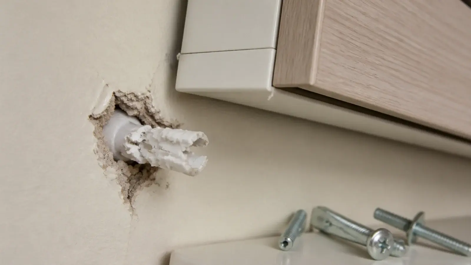 wall plug pulled loose from drywall beneath a sagging hung shoe cabinet