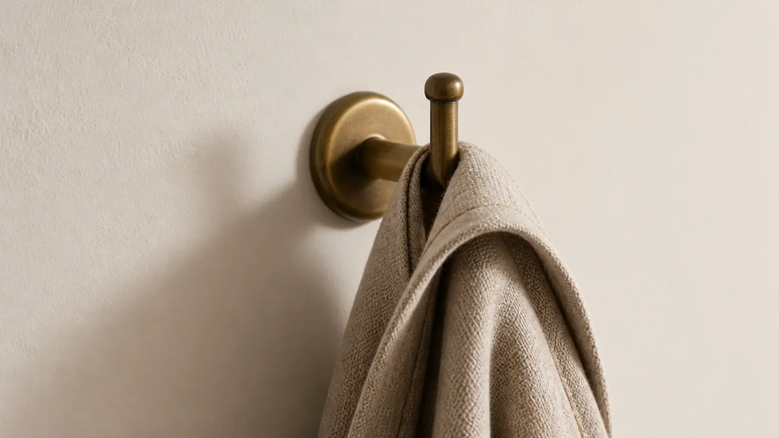single brass hook on a bare closet wall holding a linen robe