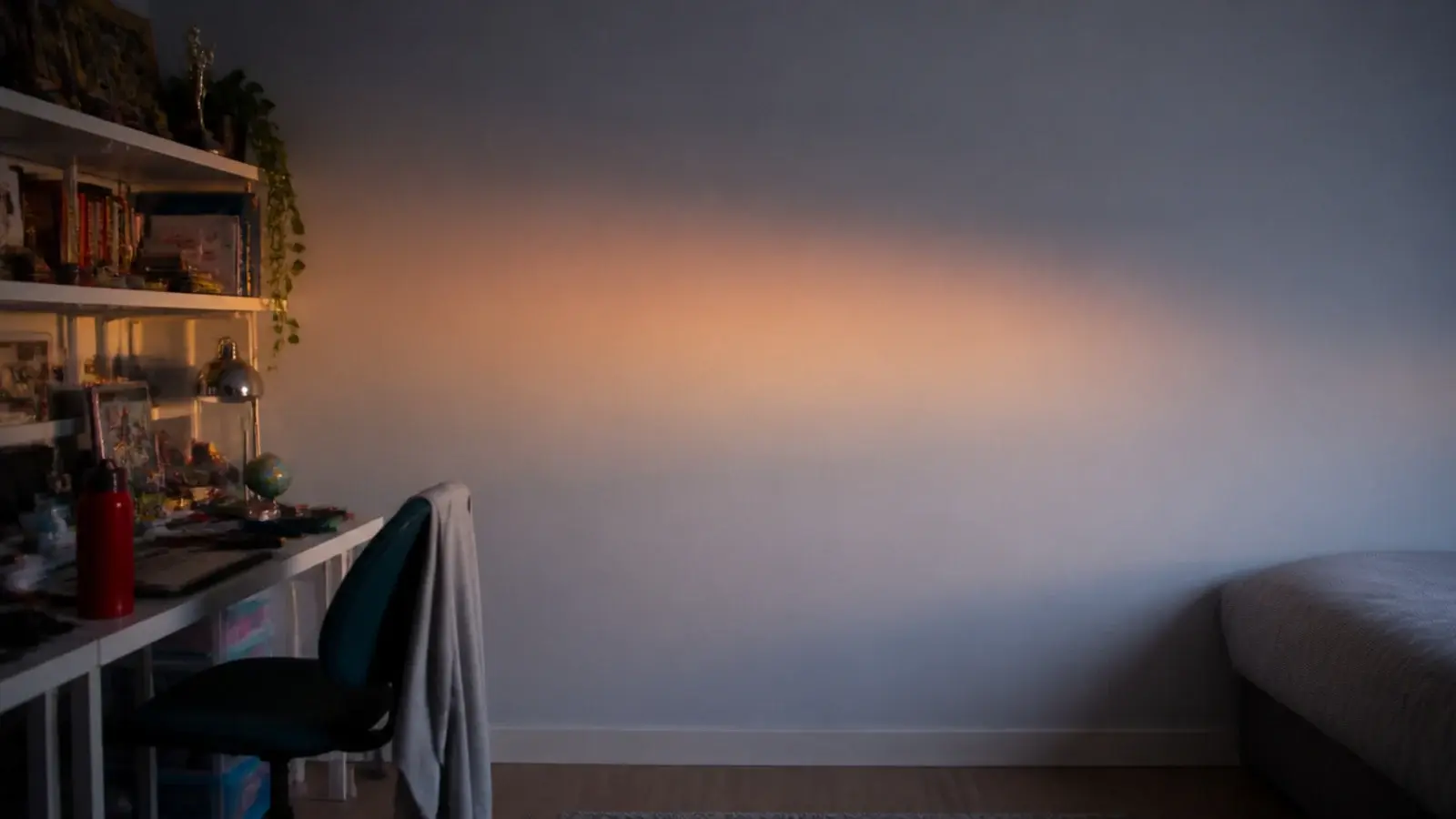 plain empty bedroom wall opposite a busy desk and shelf setup