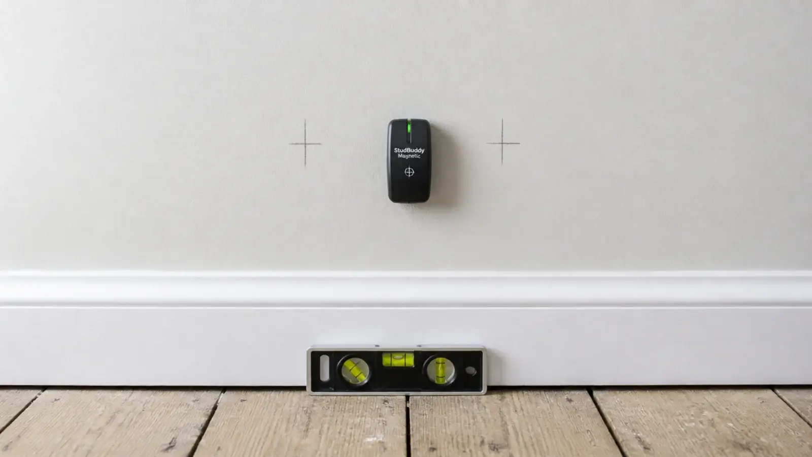 stud finder held against a bare wall beside a pencil mark and level