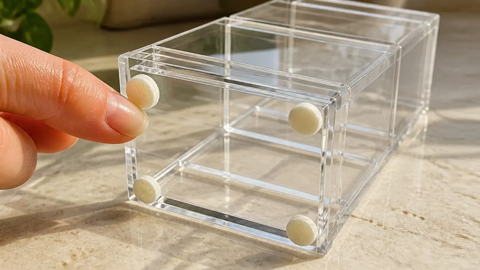 felt pads being placed under a clear acrylic organizer on stone counter