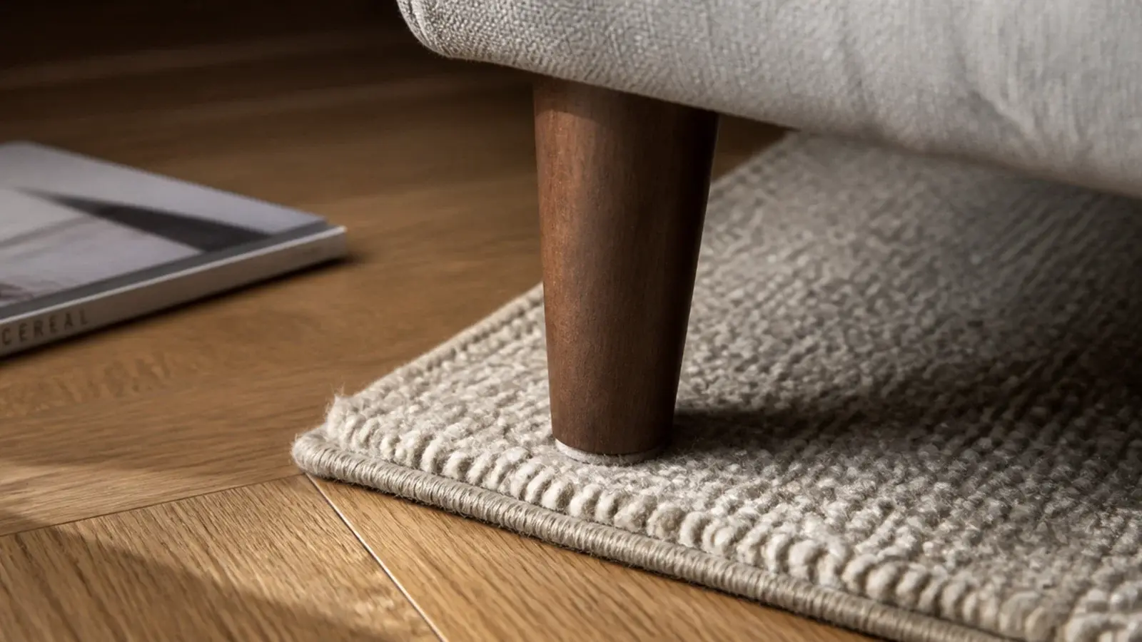 sofa leg and rug edge meeting on oak boards with a felt pad visible