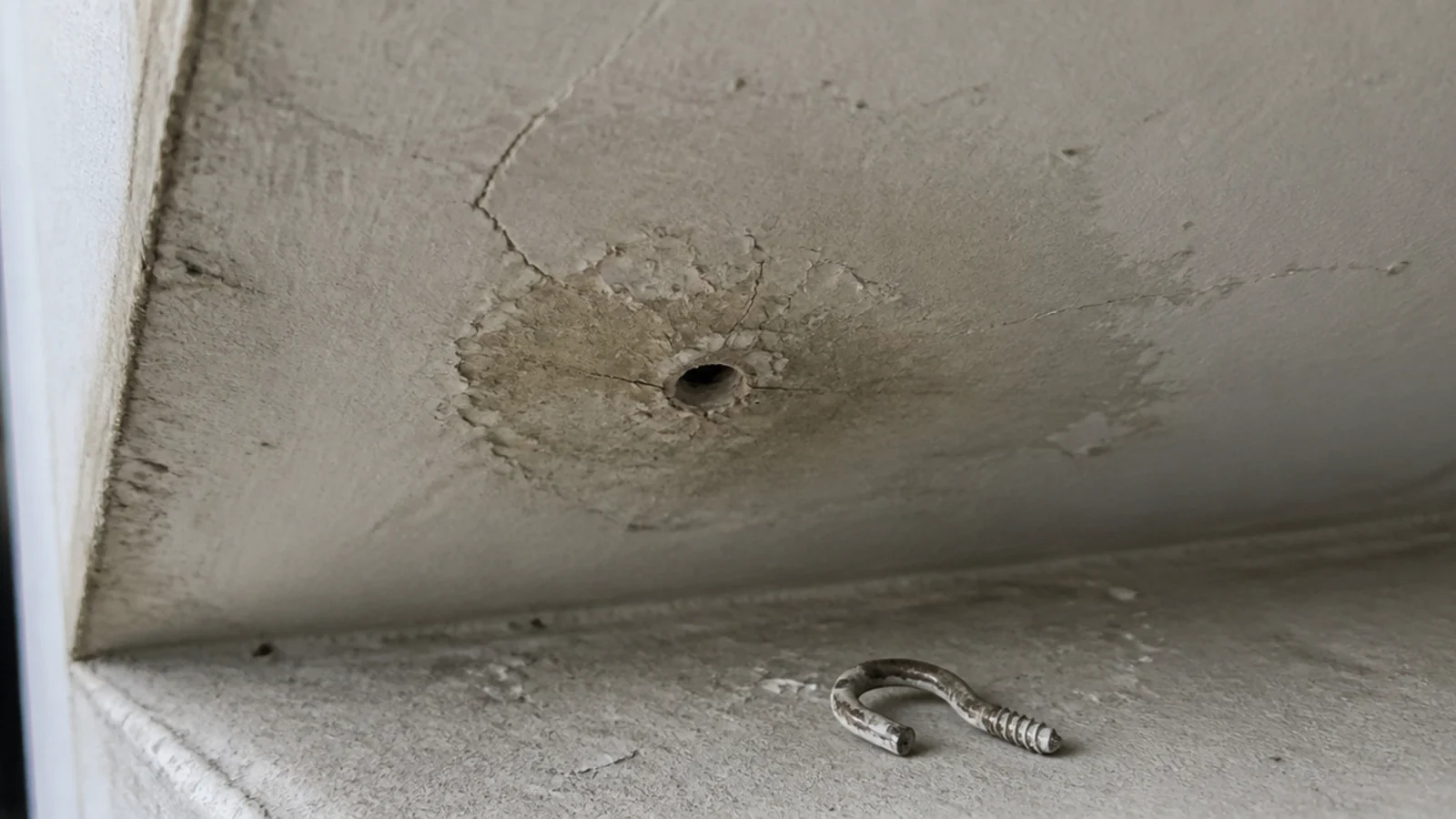 small drilled hole and cracked paint in a balcony ceiling soffit