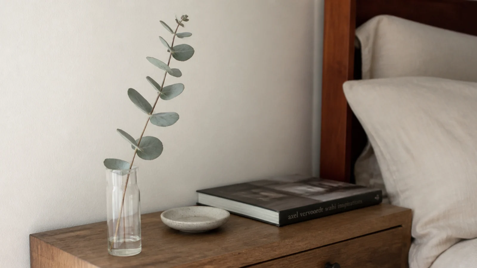 single eucalyptus sprig in a narrow glass beside a bed