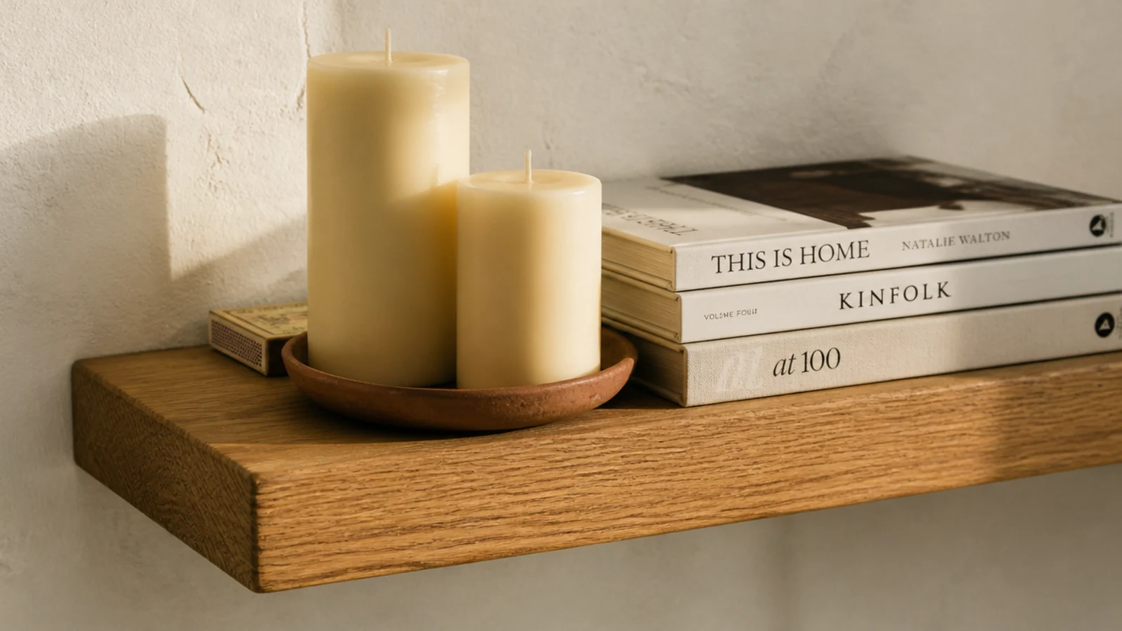 two pillar candles and a clay dish styled on an eye level bookshelf