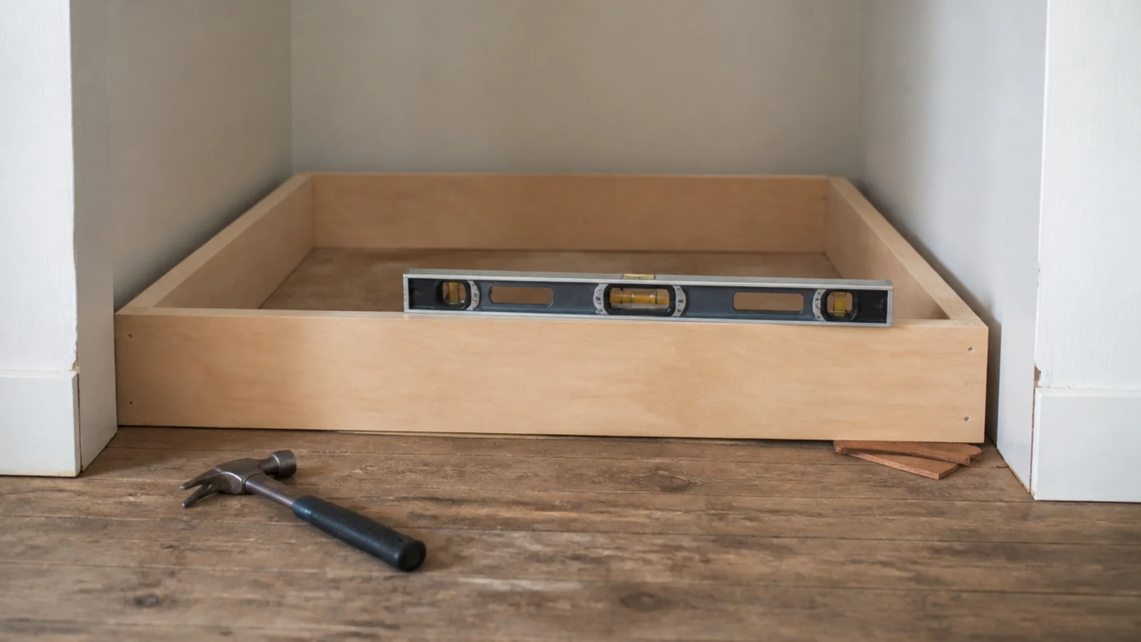 low plywood plinth base levelled with shims inside an empty alcove