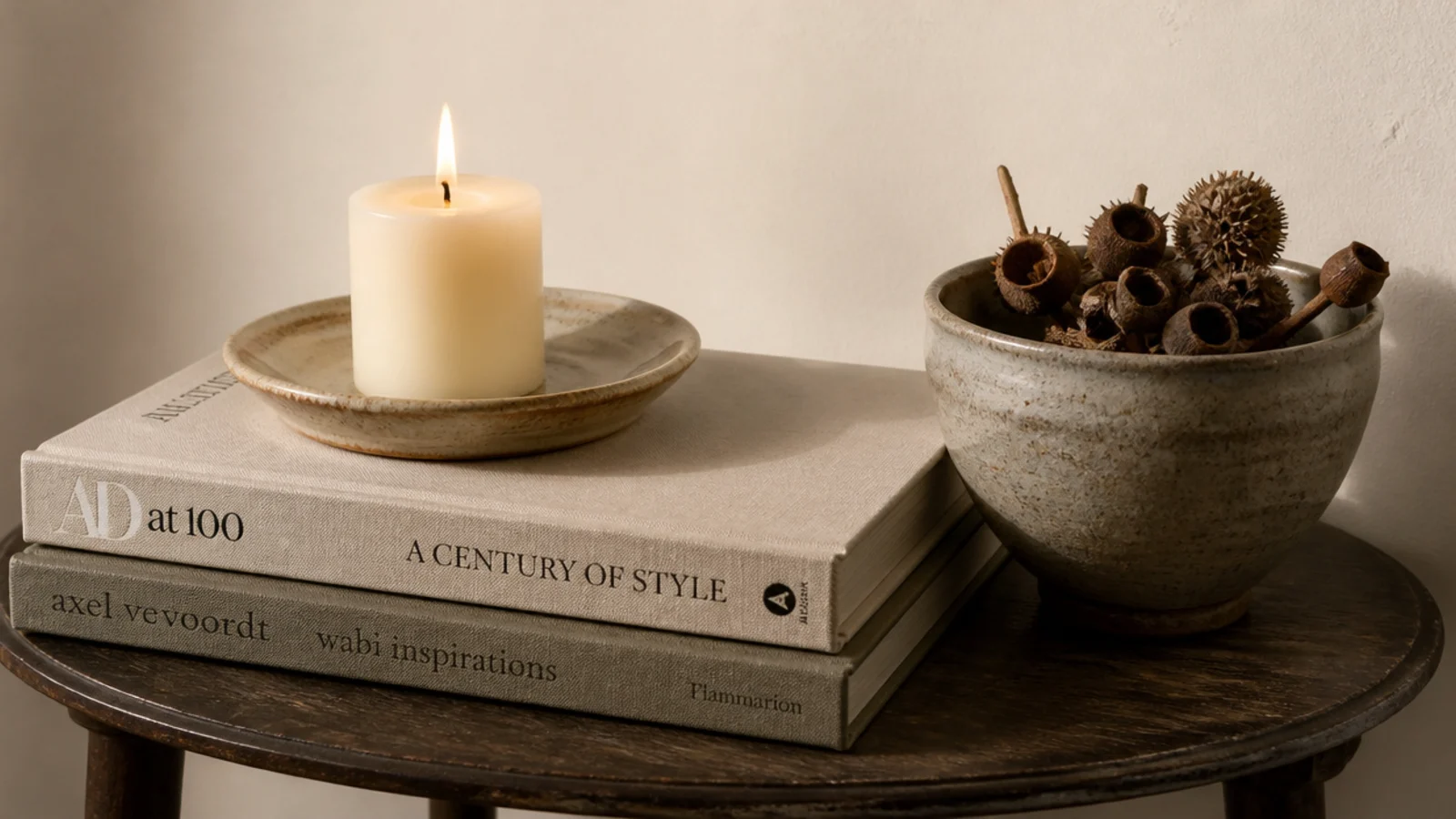 candle raised on a stack of hardback books beside a stoneware bowl