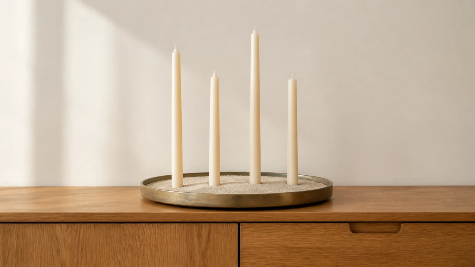 shallow tray filled with pale sand holding slim tapers upright in a cluster