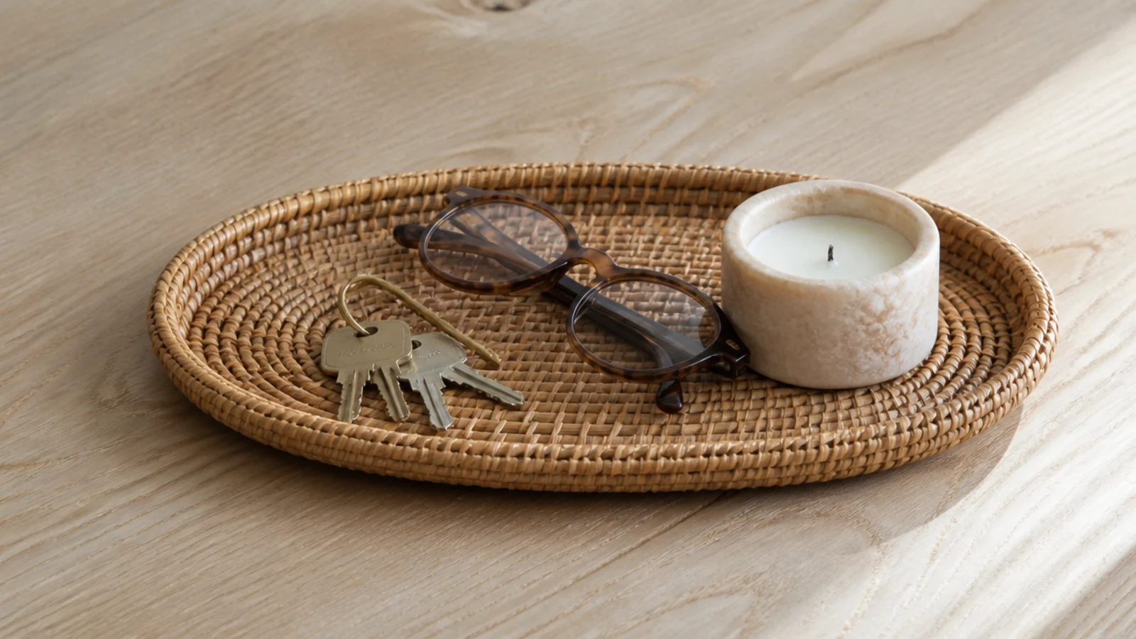 shallow rattan tray gathering keys glasses and a candle on a table