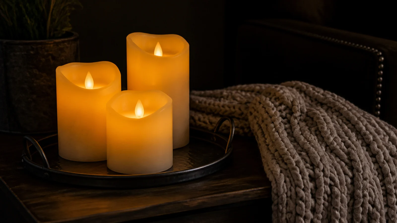 flameless LED pillar candles glowing on a tray beside a folded throw