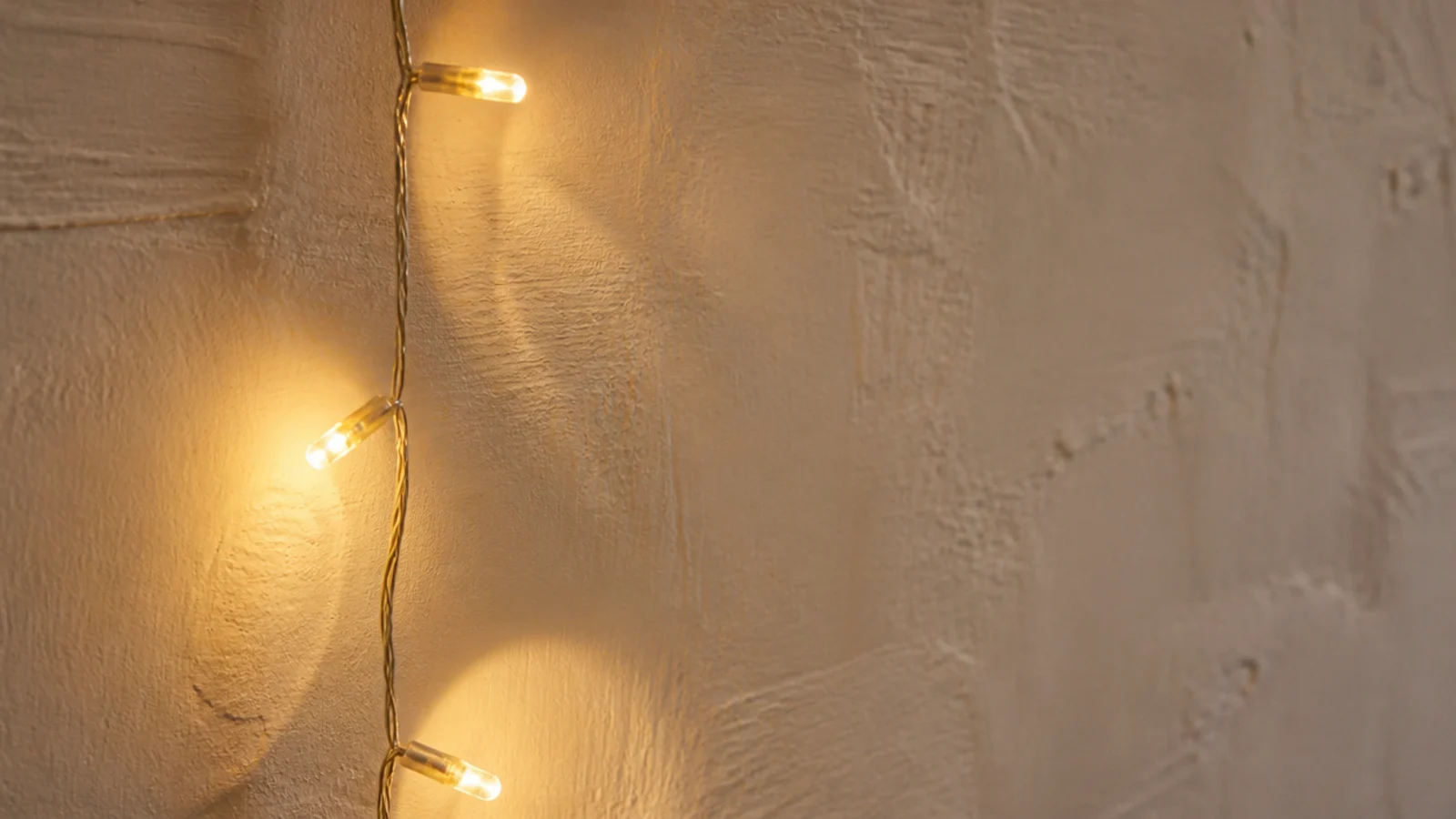 amber string light glowing against a cream limewashed bedroom wall