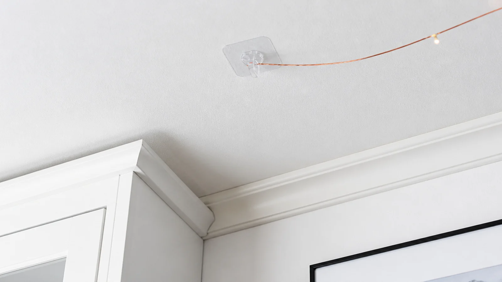 clear adhesive hook on a ceiling holding a fine light wire
