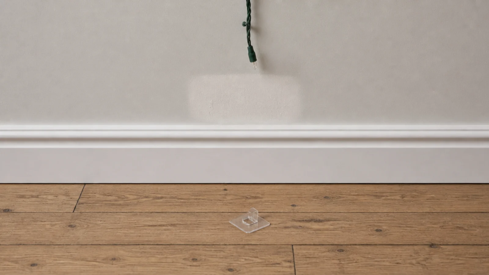 fallen adhesive clip on a floor beneath a bare wall