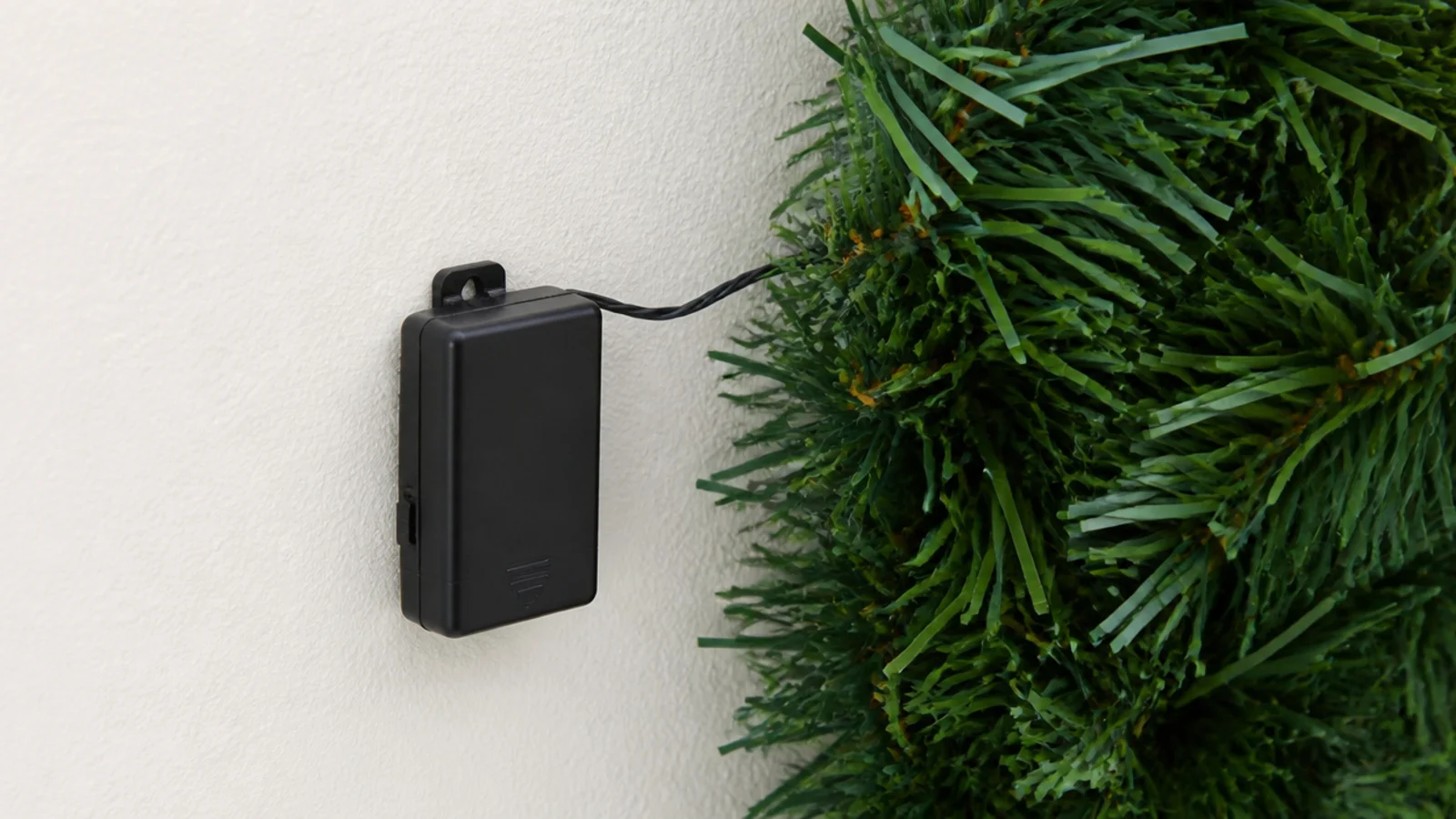 battery pack clipped to a wall outside a dense leafy garland