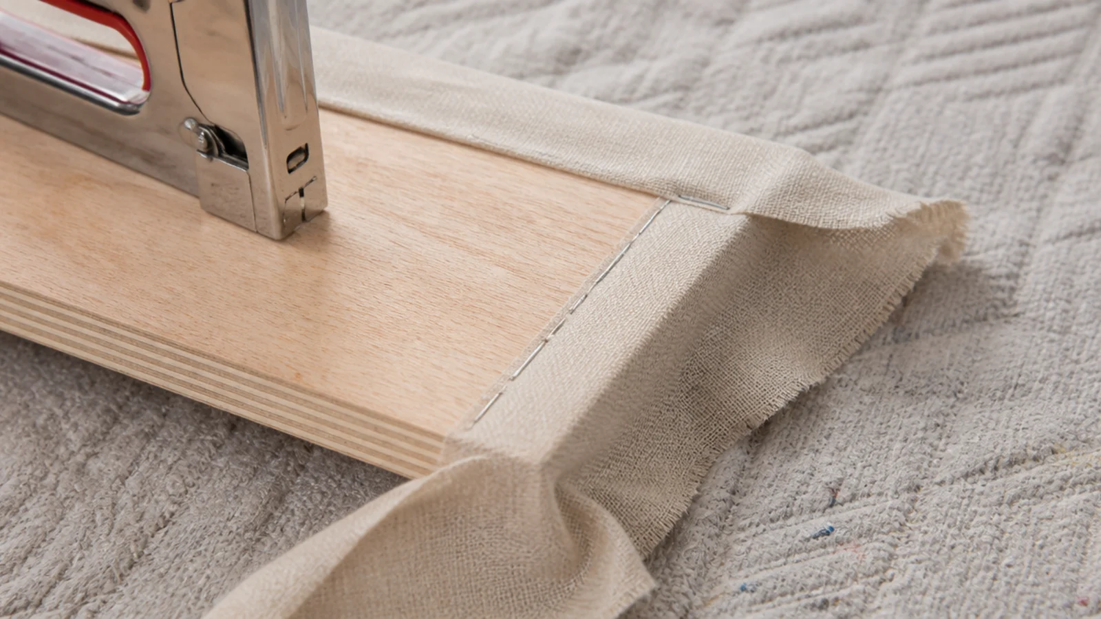staple gun tensioning linen fabric along the back of a headboard panel