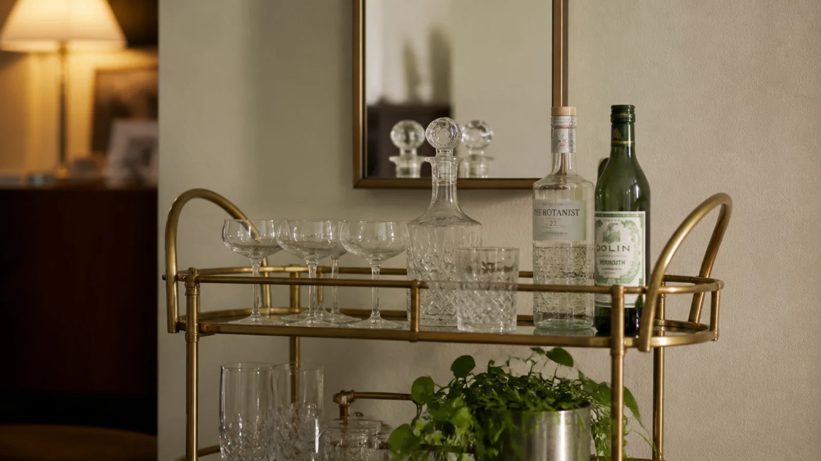 small mirror hung above a brass bar cart holding glassware and bottles
