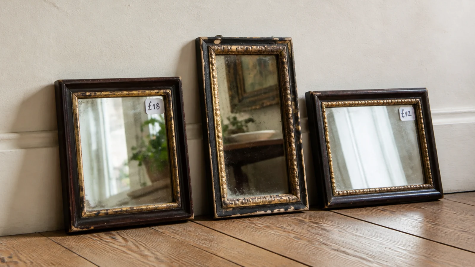 three secondhand mirrors with worn frames propped against a cream wall