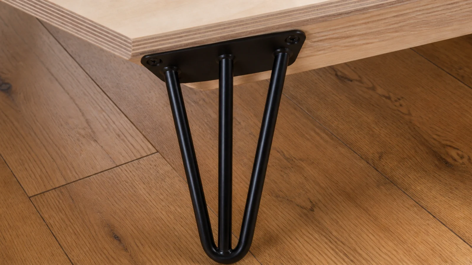 black hairpin leg bolted to the underside of a plywood desk