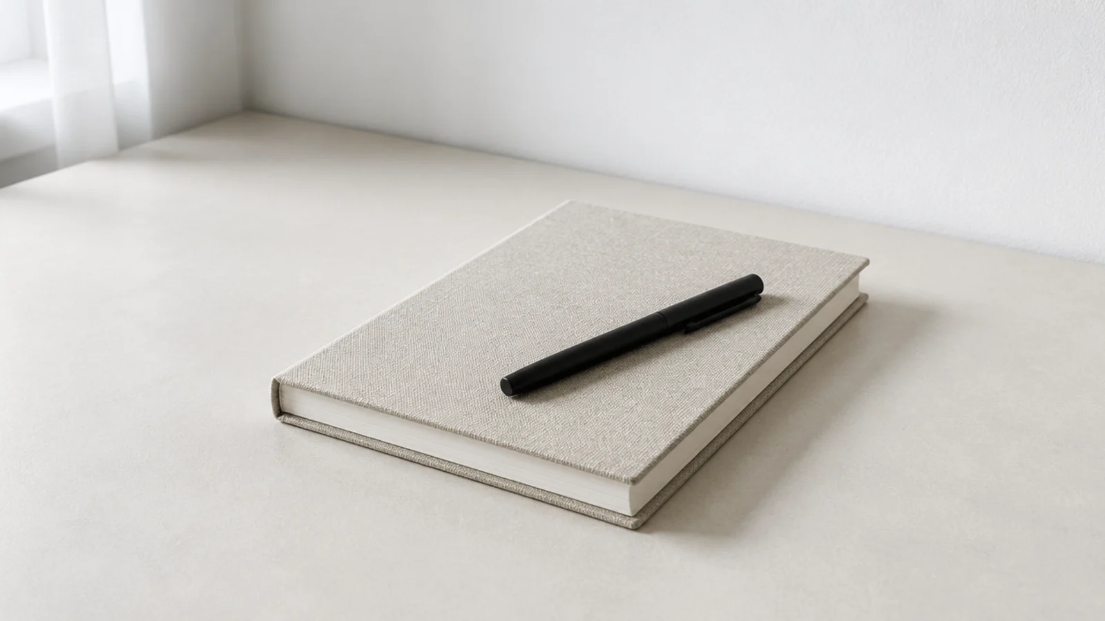 single closed notebook with one pen resting on a bare desk