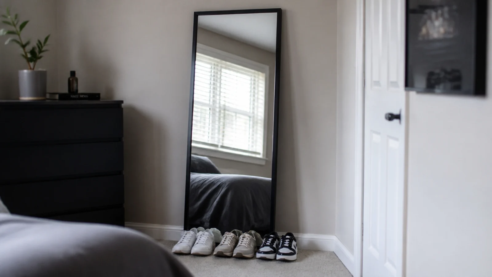 tall black framed mirror leaning against a wall reflecting a window