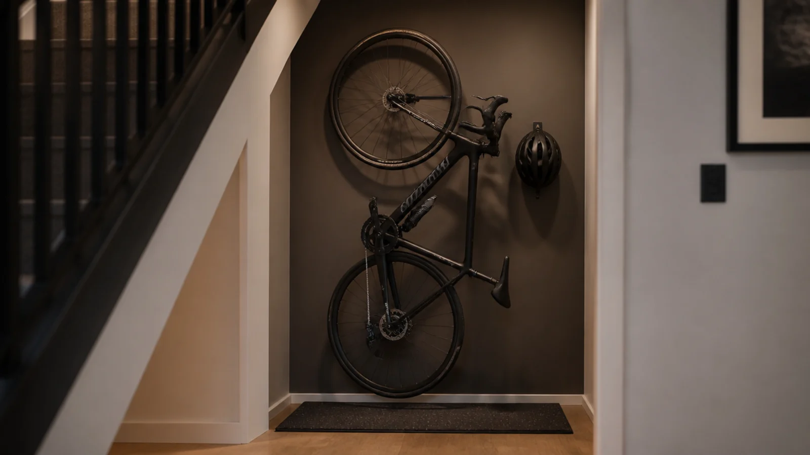 bicycle hanging vertically from a wall hook under a staircase