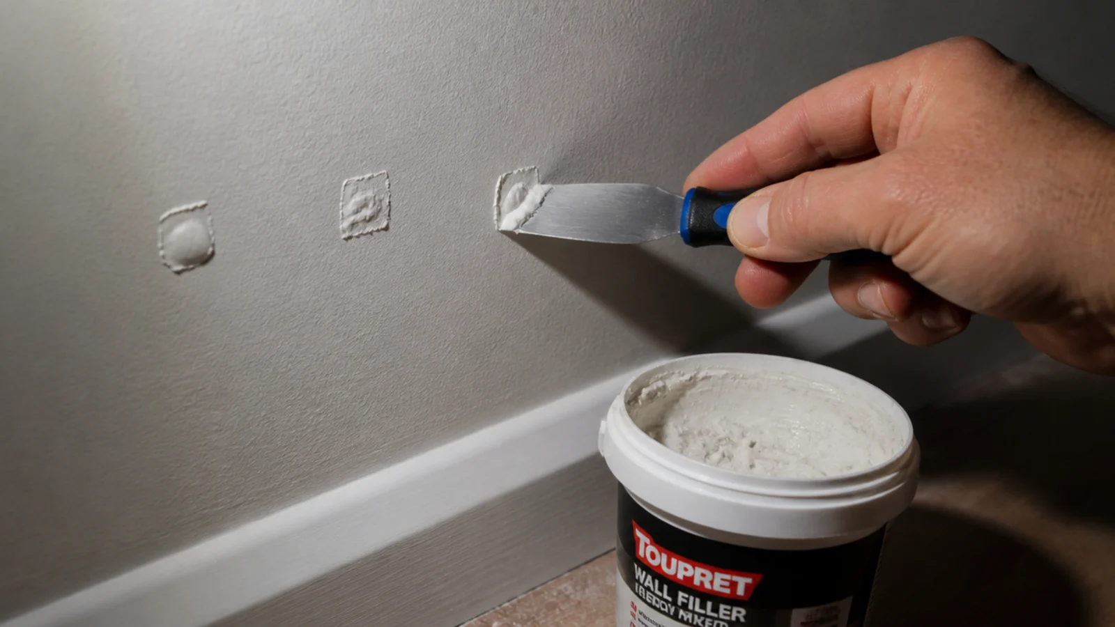 filler knife smoothing filler into a small screw hole in a painted wall